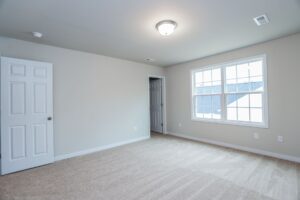 Empty carpeted room in one of the new homes in Richmond VA, featuring beige walls, large window, and two open white doors.