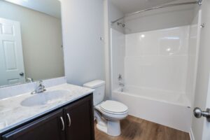 A clean bathroom in new homes in Richmond VA features a white bathtub, toilet, and a marble countertop with dark cabinet.