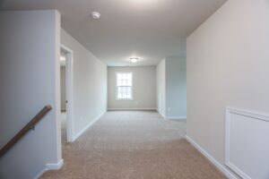 Bright, empty upstairs hallway in new homes in Richmond VA with beige carpet, white walls, and natural light from a window.