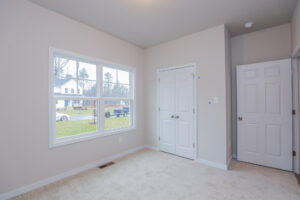 Empty room with beige carpet, white walls, large window, two closed doors, and views of Poplar Village from Lot 32.