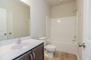 Modern bathroom in Poplar Village with a dark wood vanity, white sink, toilet, and tub-shower combo. Light walls and wood flooring.