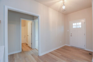 Minimalist entryway in Poplar Village with a white door, wood flooring, and a hallway leading to Lot 32s bathroom.