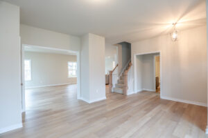 Empty room in Lot 32 with wooden floors, light walls, and recessed lighting, featuring a staircase and doorways.