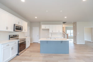 Modern kitchen in Poplar Village with white cabinets, blue island, stainless appliances, and light wood flooring.