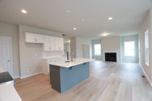 Modern kitchen and living area at Lot 32, Poplar Village, with light wood flooring, white cabinets, gray island, and fireplace.