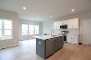 Modern kitchen on Lot 32 with island, stainless steel appliances, white cabinets, and large windows in Poplar Village.