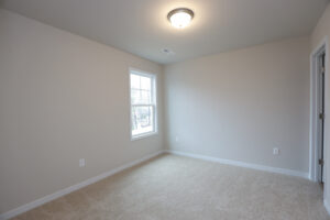 Sunlit room with beige carpet, white wall, window, and closed door in Poplar Villages Lot 32.