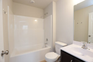 Bright bathroom in Lot 32, Poplar Village, with a white bathtub, toilet, sink, and large mirror in a minimalistic design.