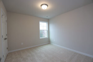 Empty room in Poplar Villages Lot 32 with beige carpet, cream walls, a window, and a ceiling light fixture.