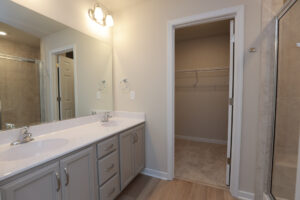 Modern bathroom in Poplar Village with double sink vanity, large mirror, and view into a carpeted walk-in closet.