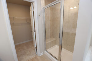 Modern bathroom with a glass-enclosed shower and beige tiles in Lot 32, next to a walk-in closet with a white door.