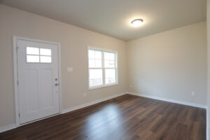 Empty room with wooden floors, a window, and a white door on Lot 31 in Poplar Village under a ceiling light.