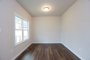 Empty room with beige walls, wooden floor, ceiling light, and large window in Poplar Villages Lot 31.
