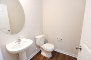 Minimalist bathroom in Poplar Village with white sink, oval mirror, and hardwood flooring.