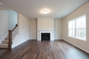 Empty living room with hardwood floors, a fireplace, a staircase, and a large window in Poplar Village.