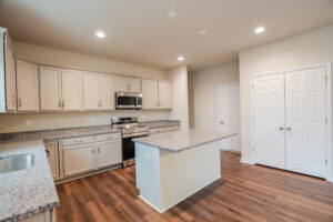 A modern kitchen in Poplar Village with white cabinets, granite countertops, stainless steel appliances, and wood flooring.