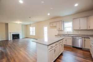 Spacious open-concept kitchen and living area in Poplar Village, featuring wooden floors, white cabinets, and a fireplace.