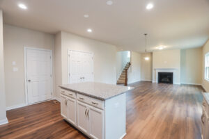 Open living room with wood floors, kitchen island, and fireplace in Lot 31 of Poplar Village. Bright with neutral walls and lights.