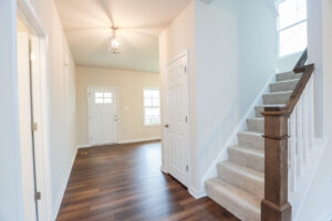 Bright entryway at Lot 31 with a white door, carpeted stairs, and hardwood floors in Poplar Village.
