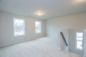 Empty room in Poplar Villages Lot 31: beige walls, carpeted floor, three windows, and a staircase railing.