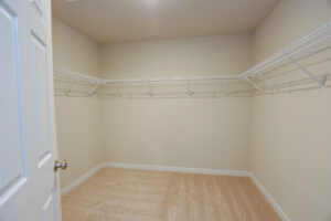 Empty walk-in closet with beige walls, carpeted floor, and white wire shelves in Poplar Villages Lot 31.
