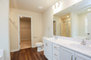 Modern bathroom in Poplar Village with dual sinks, a large mirror, wooden floor, and a walk-in closet. Lot 31.