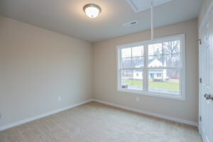 Empty room in Poplar Village, Lot 31, with beige carpet, white walls, a window view, and a ceiling light fixture.
