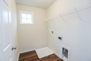 Empty laundry room with a window, wall shelf, and water connections on light-colored walls in Poplar Villages Lot 31.