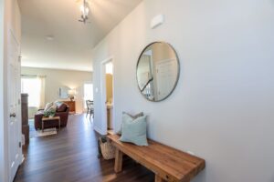 A hallway in new homes in Richmond VA with a wooden bench, pillows, basket, mirror, and view into a bright living room.