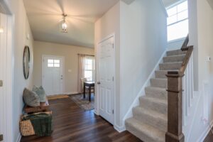 Bright entryway in new homes in Richmond VA, with white front door, carpeted stairs, hardwood floors, baskets and cushions.