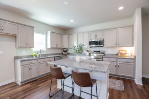 Modern kitchen in new homes in Richmond VA with gray cabinets, granite counters, and two brown island stools.