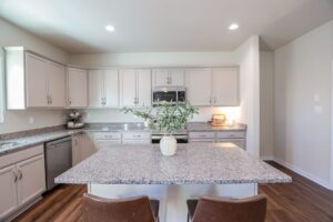 Modern kitchen in new homes in Virginia with white cabinets, granite countertops, and a vase with greenery on the island.