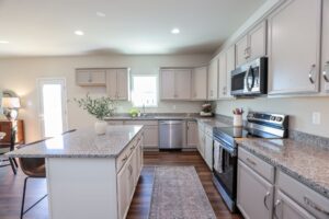 Modern kitchen in new homes in Richmond VA featuring gray cabinets, granite countertops, and a central island.