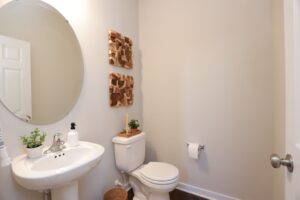 A small bathroom in new homes in Richmond VA with a pedestal sink, round mirror, wall art, and decorative plants.