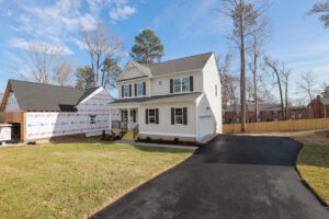 A two-story white house with a new driveway stands on Lot 31, next to a partially constructed Poplar Village building.