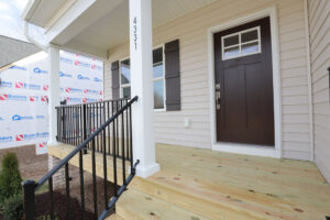 A newly constructed front porch in Poplar Village, Lot 31, features wooden steps and a dark brown door.