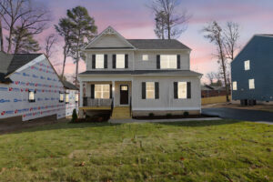 Nestled in Poplar Village, a two-story house on Lot 31 stands aglow at dusk, beside a finished and a budding home.