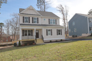 A modern two-story house with a front porch in Poplar Village, nestled on a grassy lawn near Lot 31s blue neighbor.