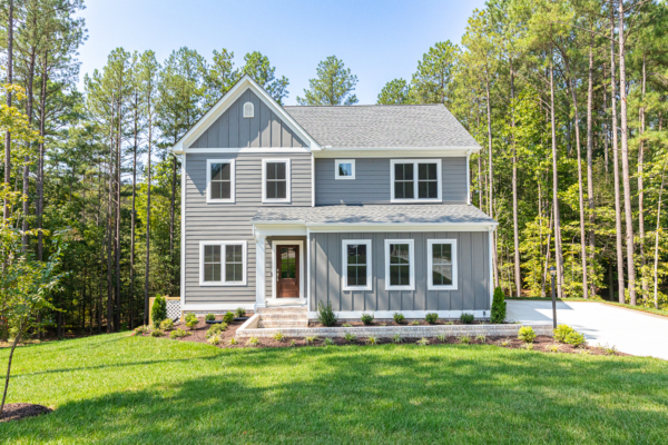 Nestled in Poplar Village, a gray two-story house with a front lawn is surrounded by tall trees under a clear blue sky.