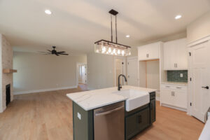 Modern kitchen with island, farmhouse sink, and wood flooring in Poplar Village. Open layout, white cabinets, pendant light.