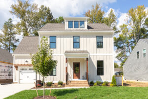 The two-story modern house on Lot 5 in Haley Meadows features a sleek white exterior, a spacious garage, and a charming small tree gracing the front yard on this sunny day.
