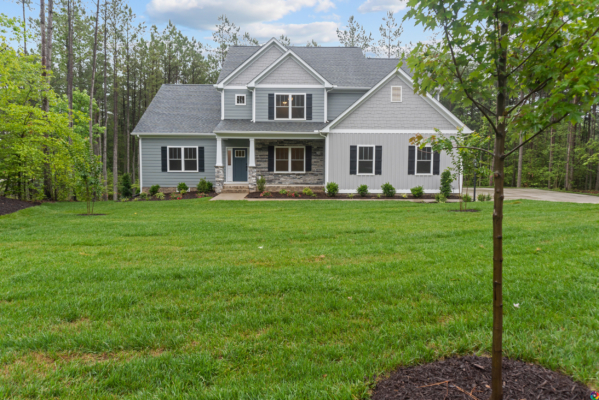 The large gray house in Scotchtown Estates boasts a manicured lawn, surrounded by trees, under a partly cloudy sky.