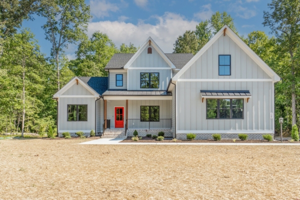 Nestled in Scotchtown Estates, this modern two-story house boasts grey siding, a striking red front door, and large windows, all surrounded by lush trees.