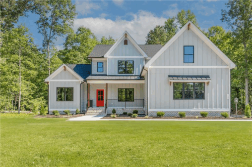 Modern farmhouse in Scotchtown Estates with gray siding, black roof, large windows, and a bright red front door.