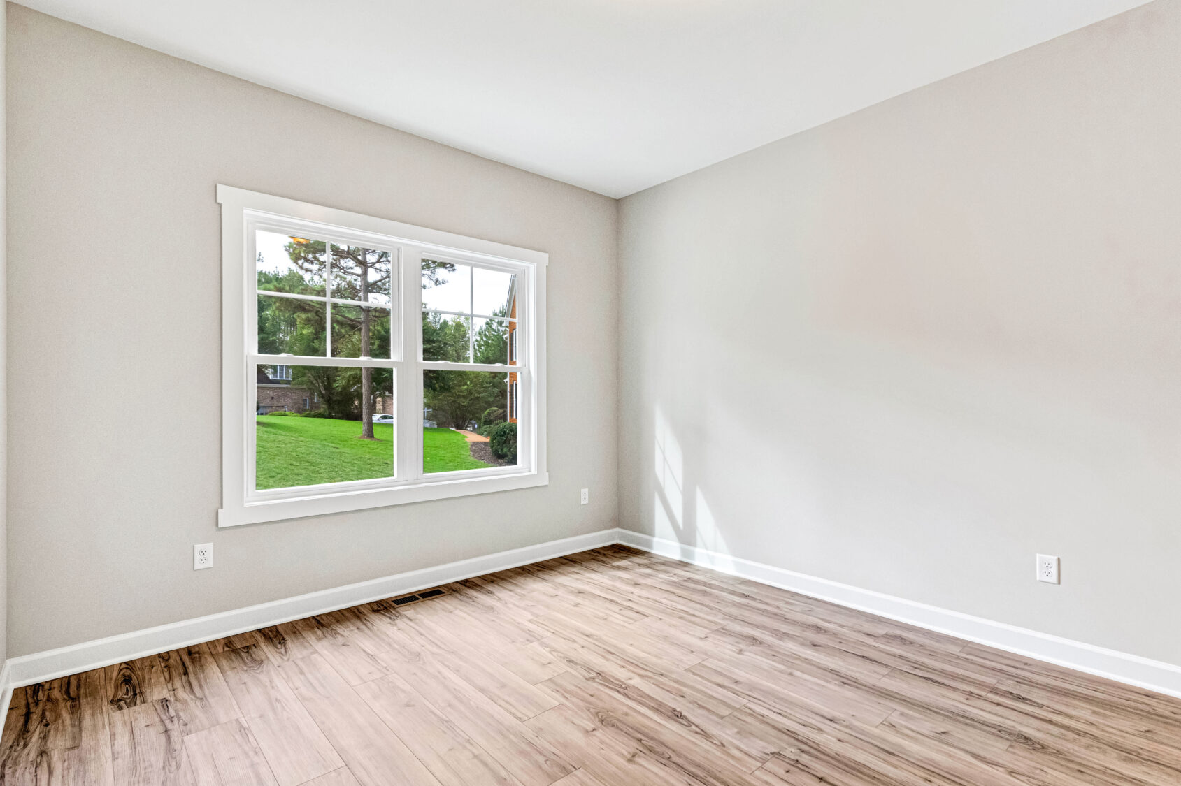 Empty room with light wood flooring, a large window, and neutral-colored walls, overlooking a green yard.