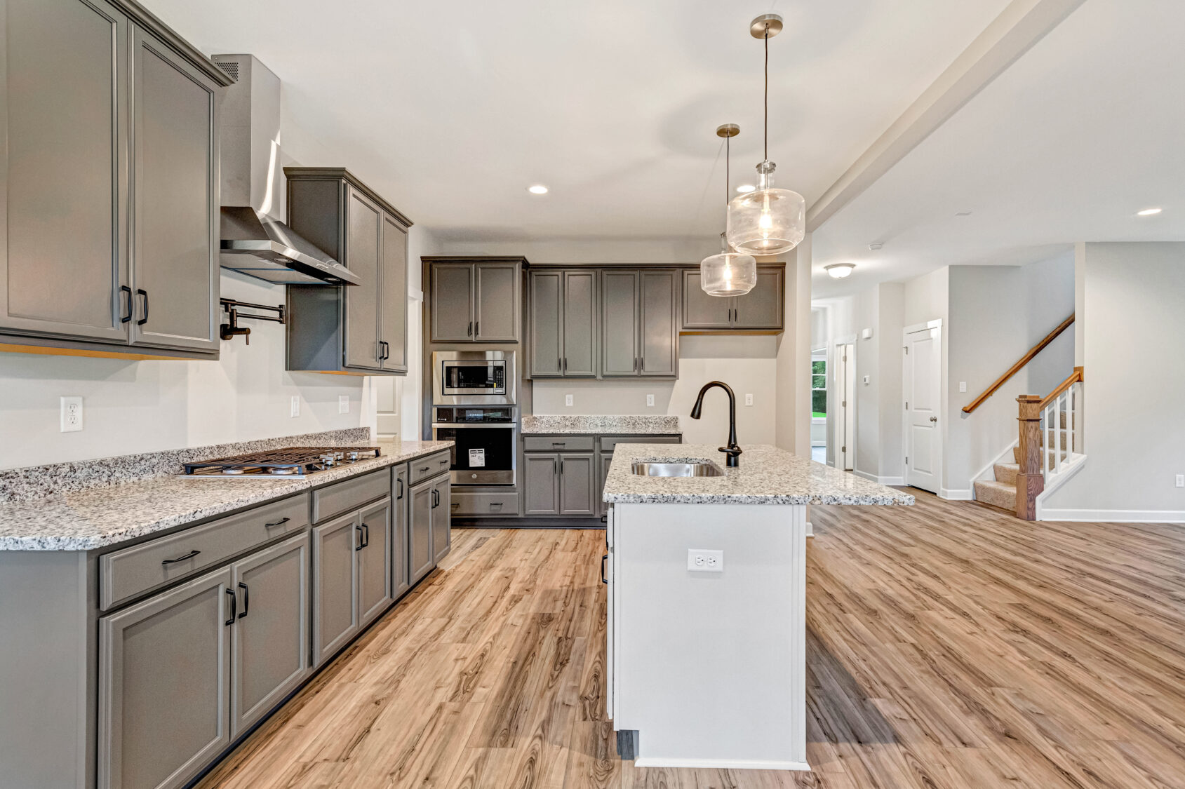 Modern kitchen with gray cabinets, granite countertops, island sink, and wood flooring in open-concept home.