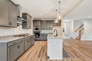 Modern kitchen with gray cabinets, granite countertops, island sink, and wood flooring in open-concept home.