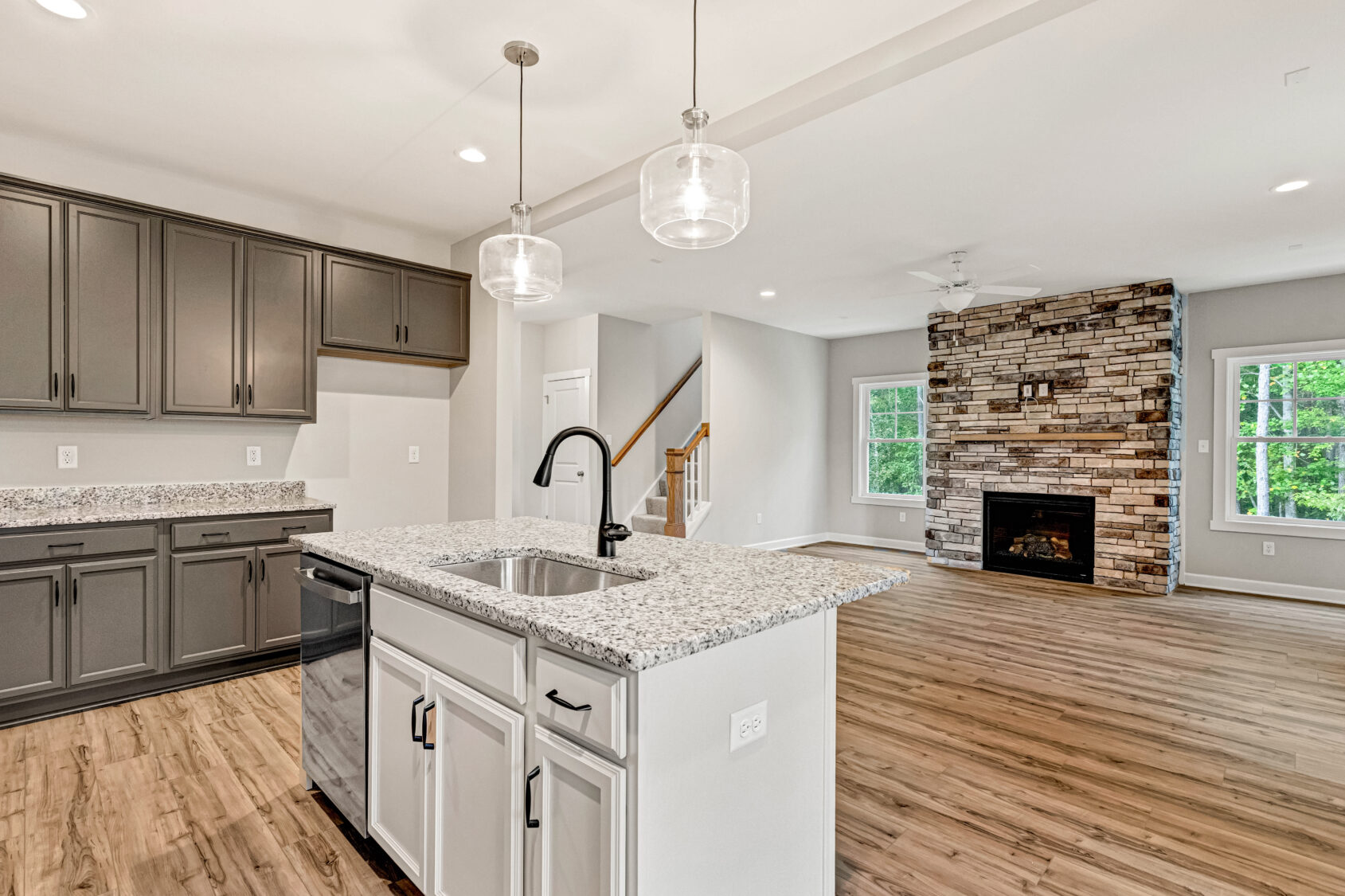 Modern kitchen with gray cabinets, island sink, and open living area featuring a stone fireplace and wood floors.