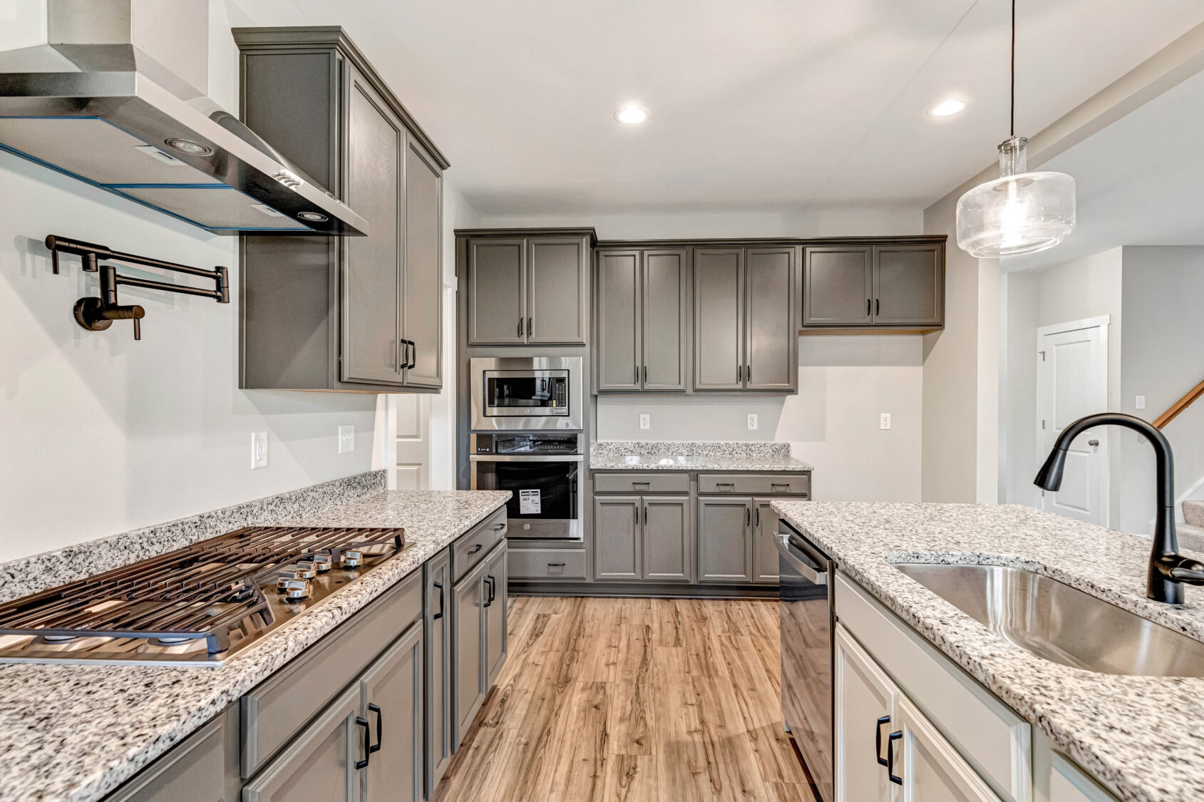 Modern kitchen with gray cabinets, granite countertops, gas stovetop, built-in ovens, and wood flooring.