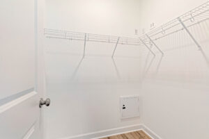 Empty walk-in closet with white wire shelves, white walls, and light wood flooring.